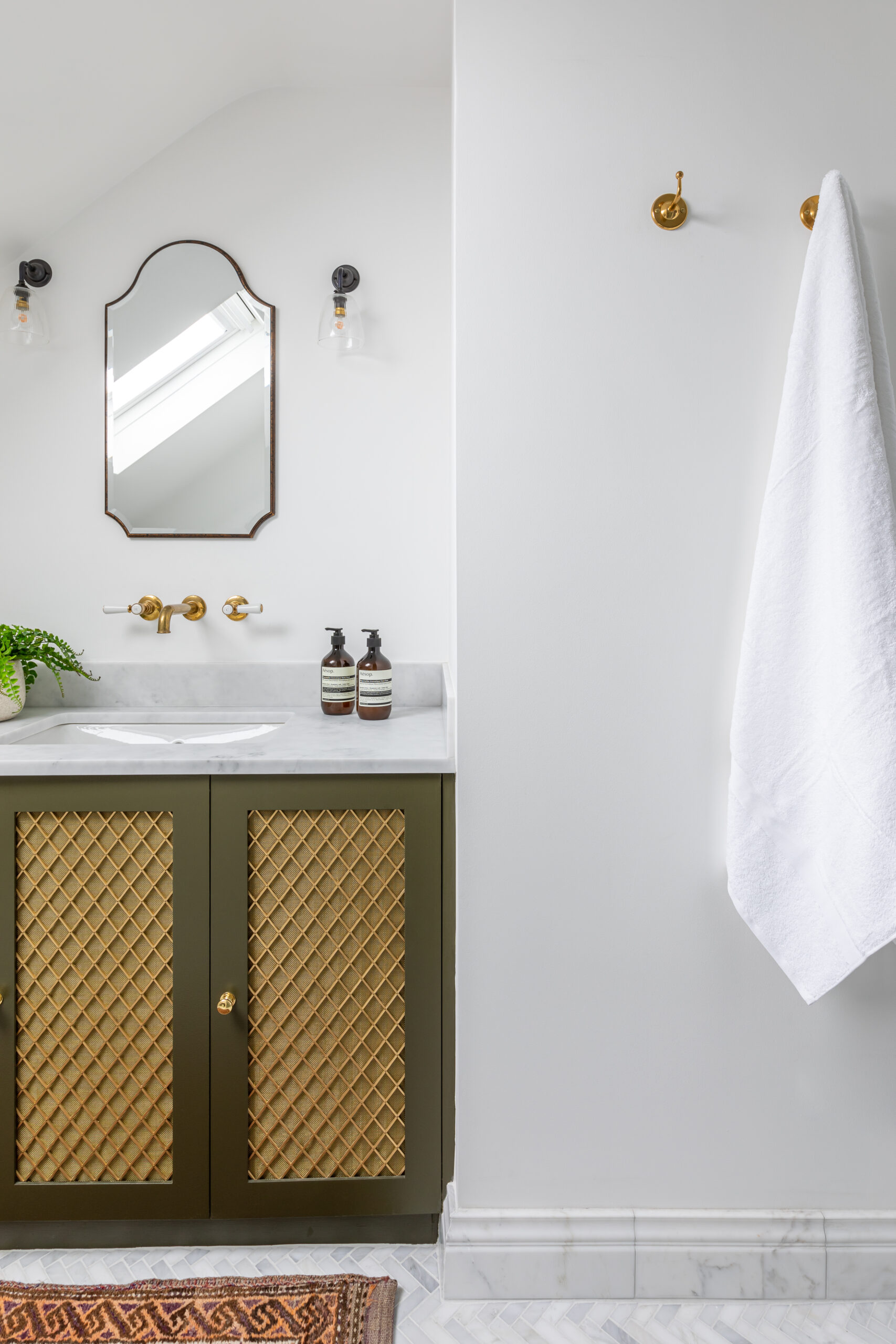 Olive green hand painted bespoke bathroom vanity with brass mesh, marble taps and curved mirror above with fluted glass wall lights.