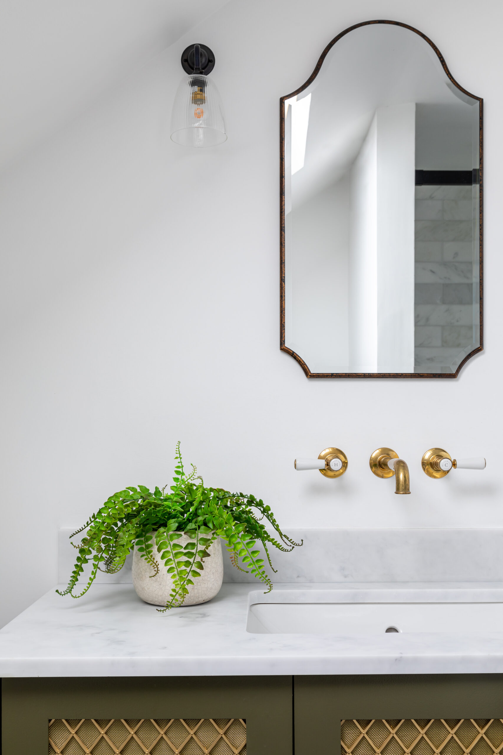 Marble topped bespoke vanity with un-lacquered brass taps and slim black oval framed mirror above.