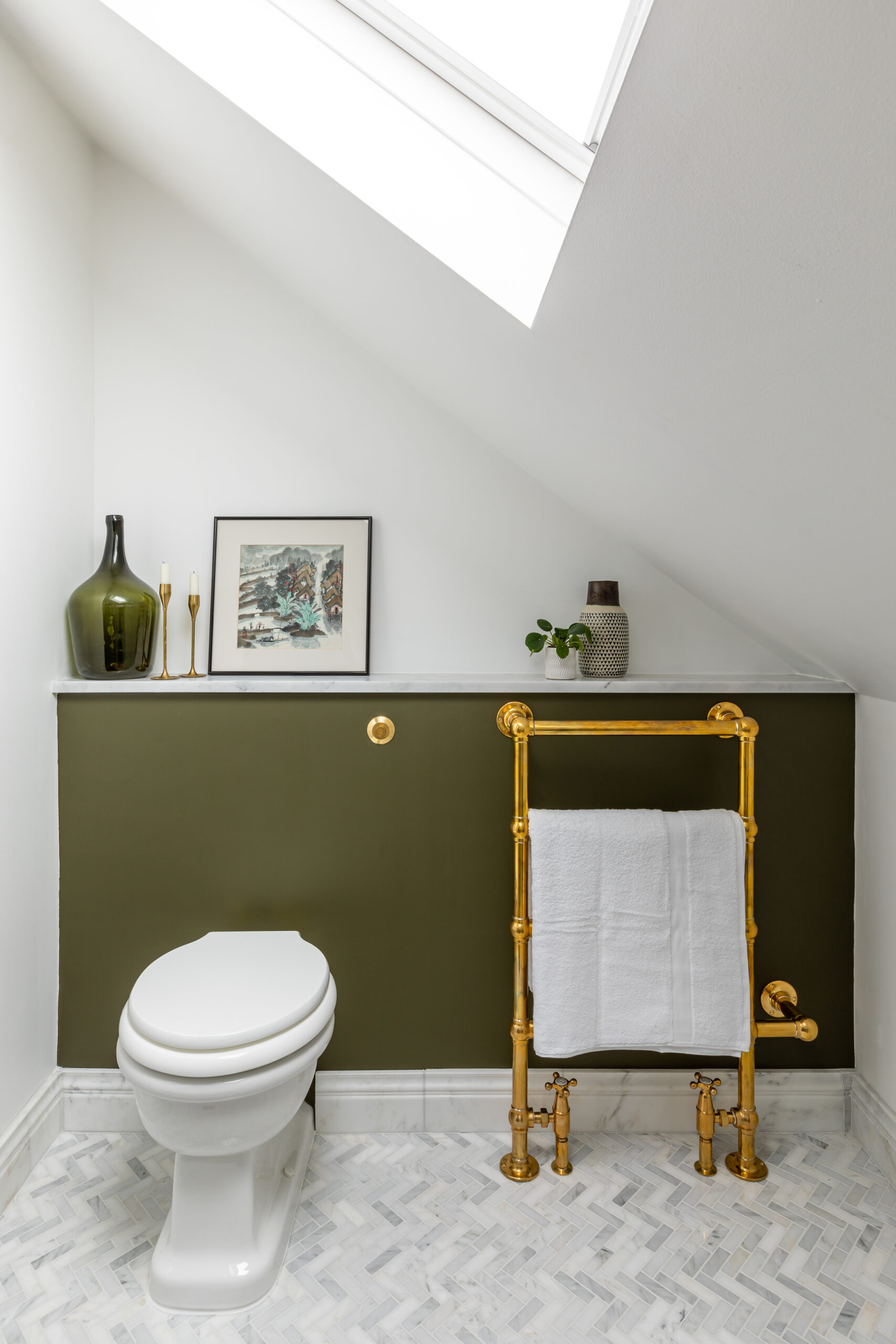 Olive green painted concealed cistern in bathroom with un lacquered brass towel rail