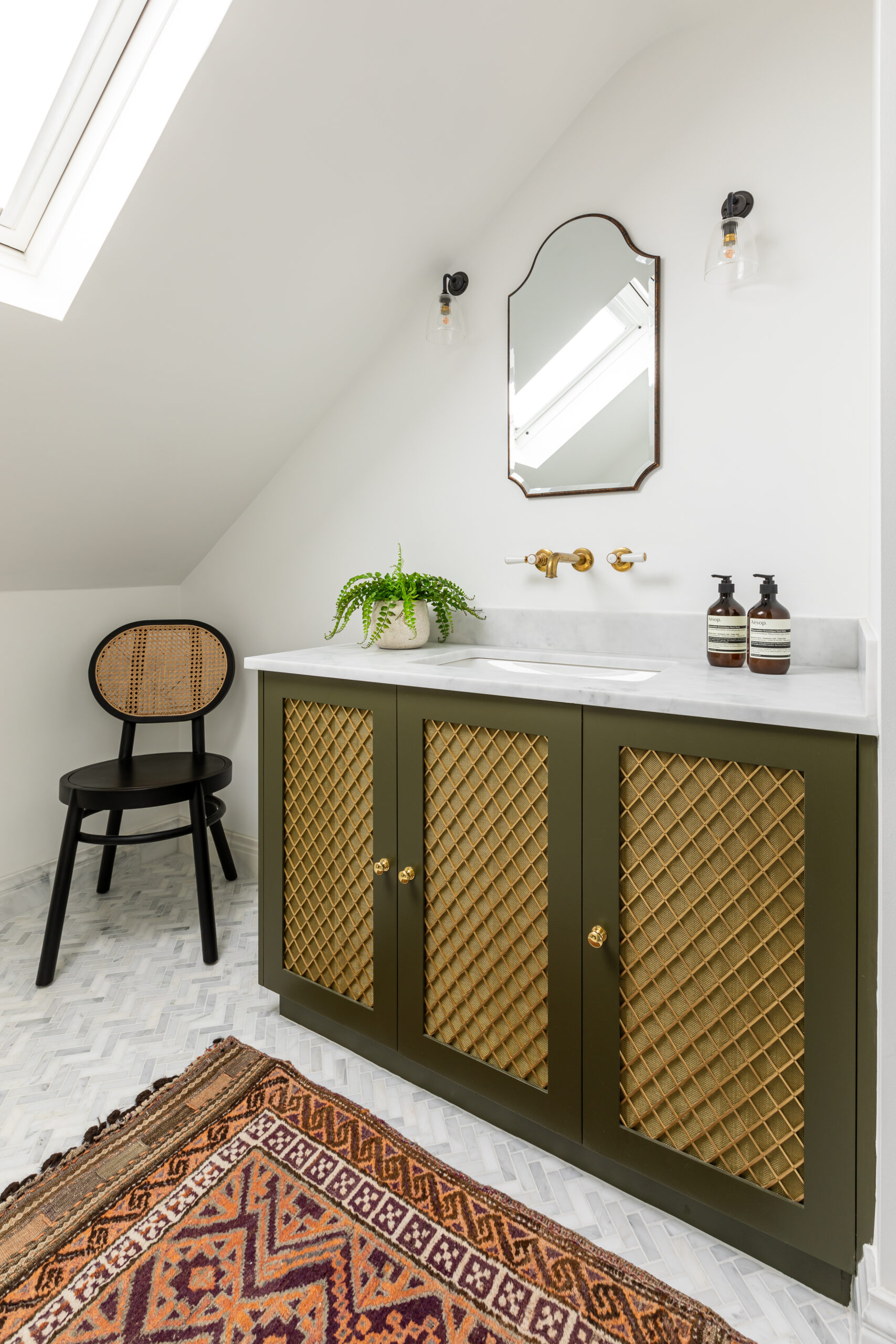 Olive green bespoke vanity with brass grill, marble top and brass taps sitting on a marble herringbone tiled floor.