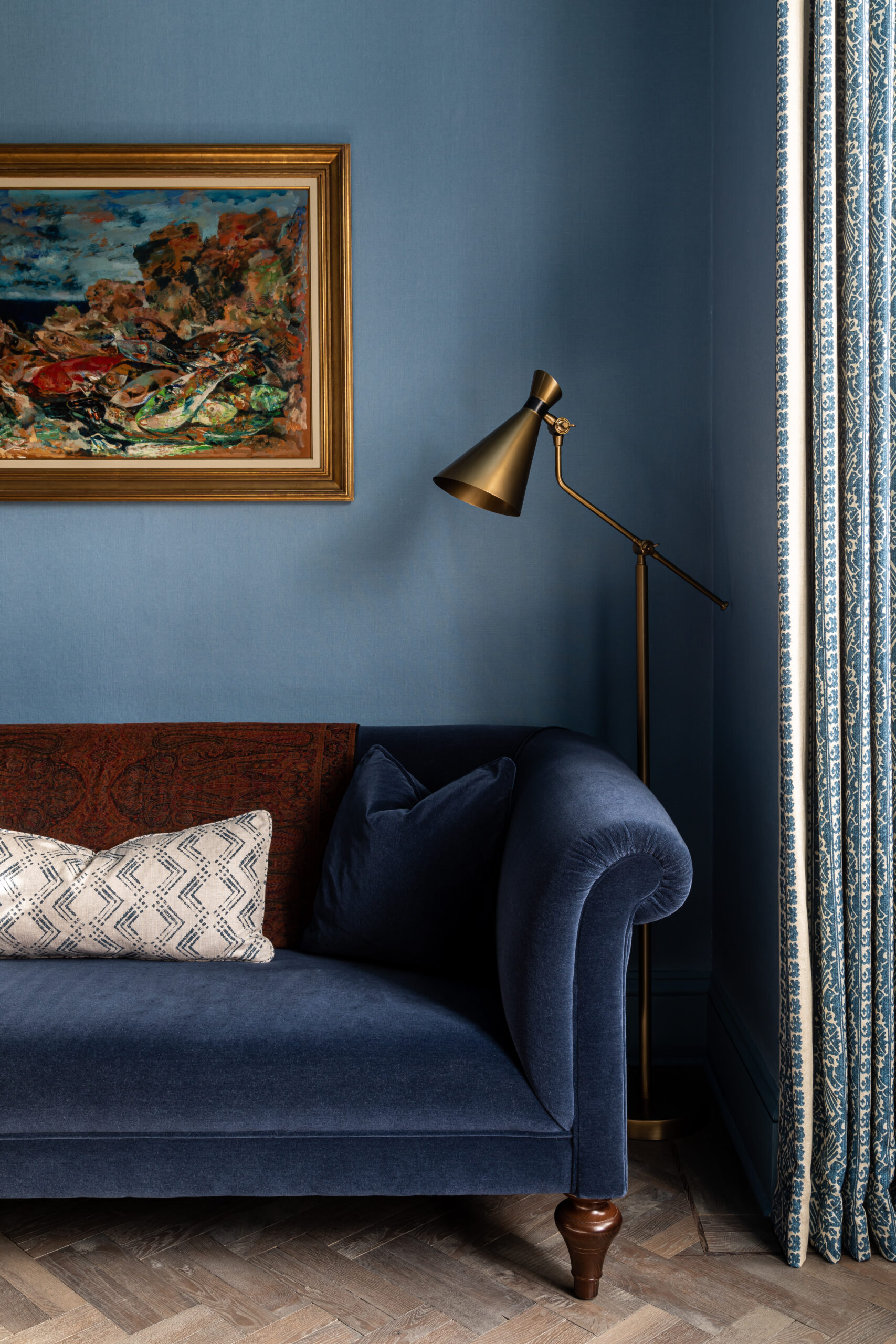 Blue mohair velvet sofa with colourful fish oil painting on blue linen walls.