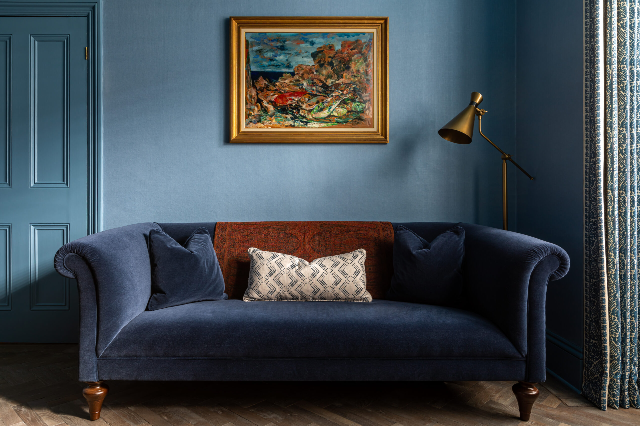 Blue mohair velvet sofa with colourful fish oil painting on blue linen walls.
